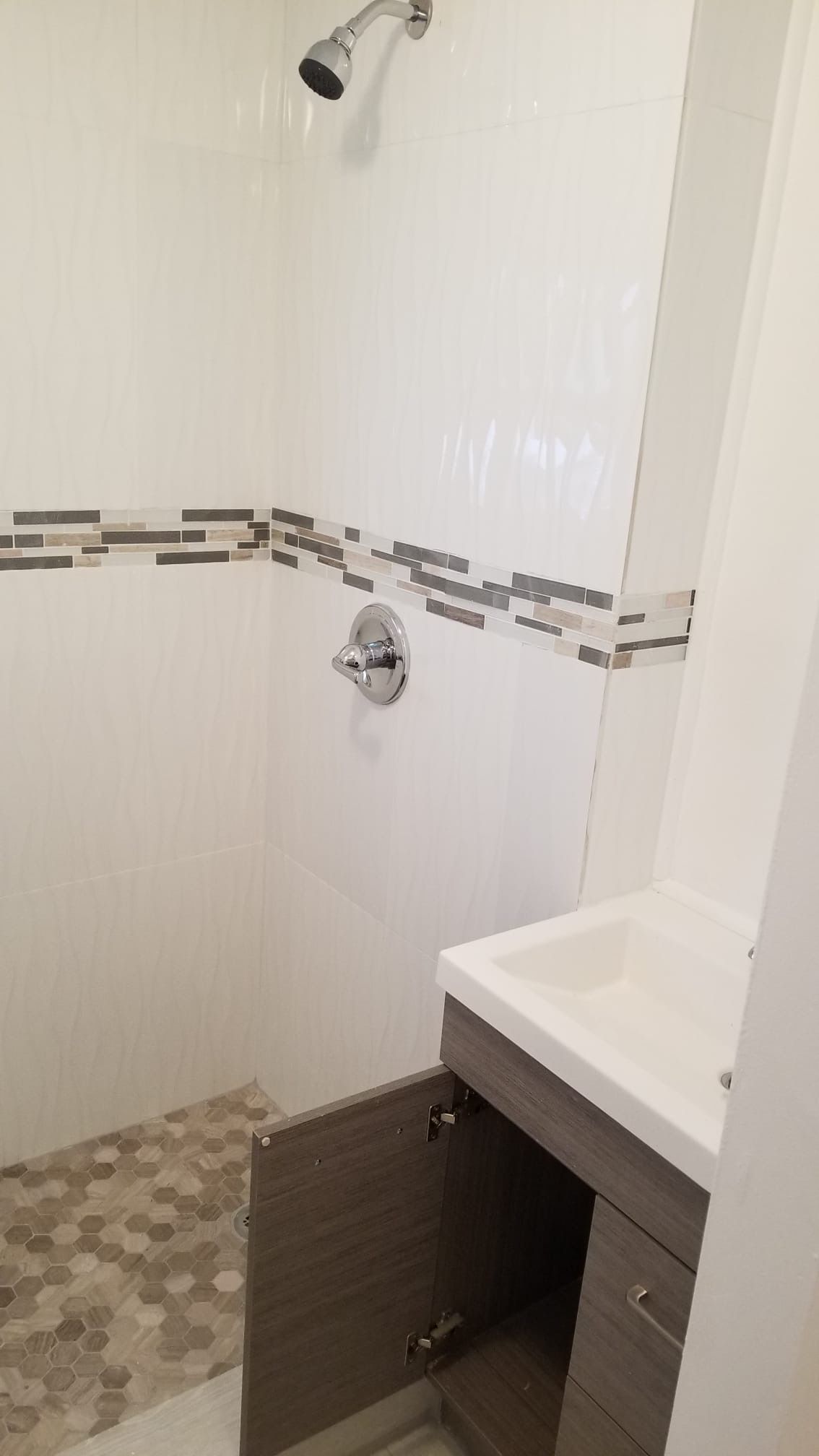 Bathroom with shower, vanity. White walls, decorative tile, grey and white sink cabinet, hexagon floor tile.