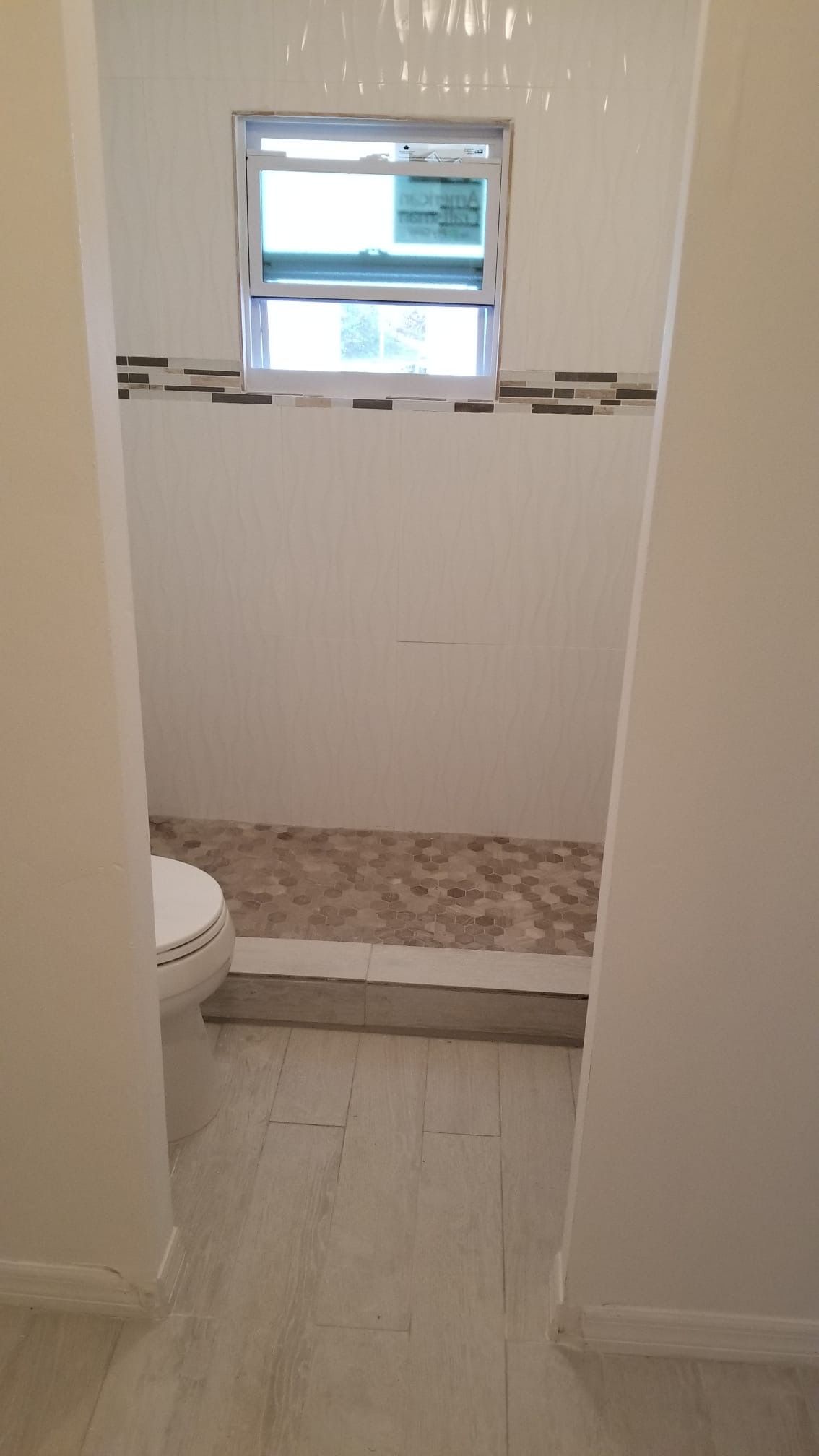 Bathroom with white walls, a window, and a pebble-stone shower floor. A toilet is visible.