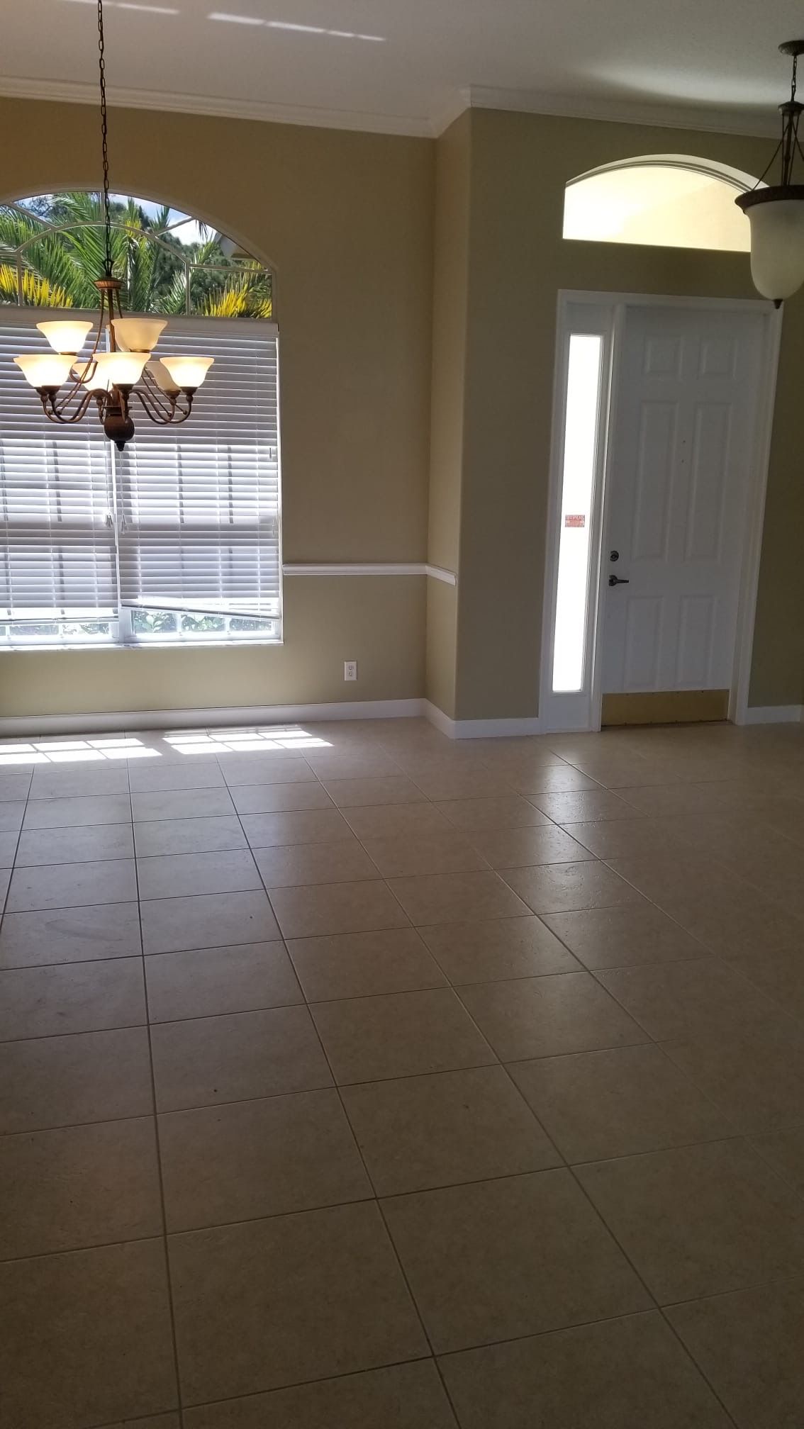 Empty room with tiled floor, arched window, and front door; tan walls and white trim.