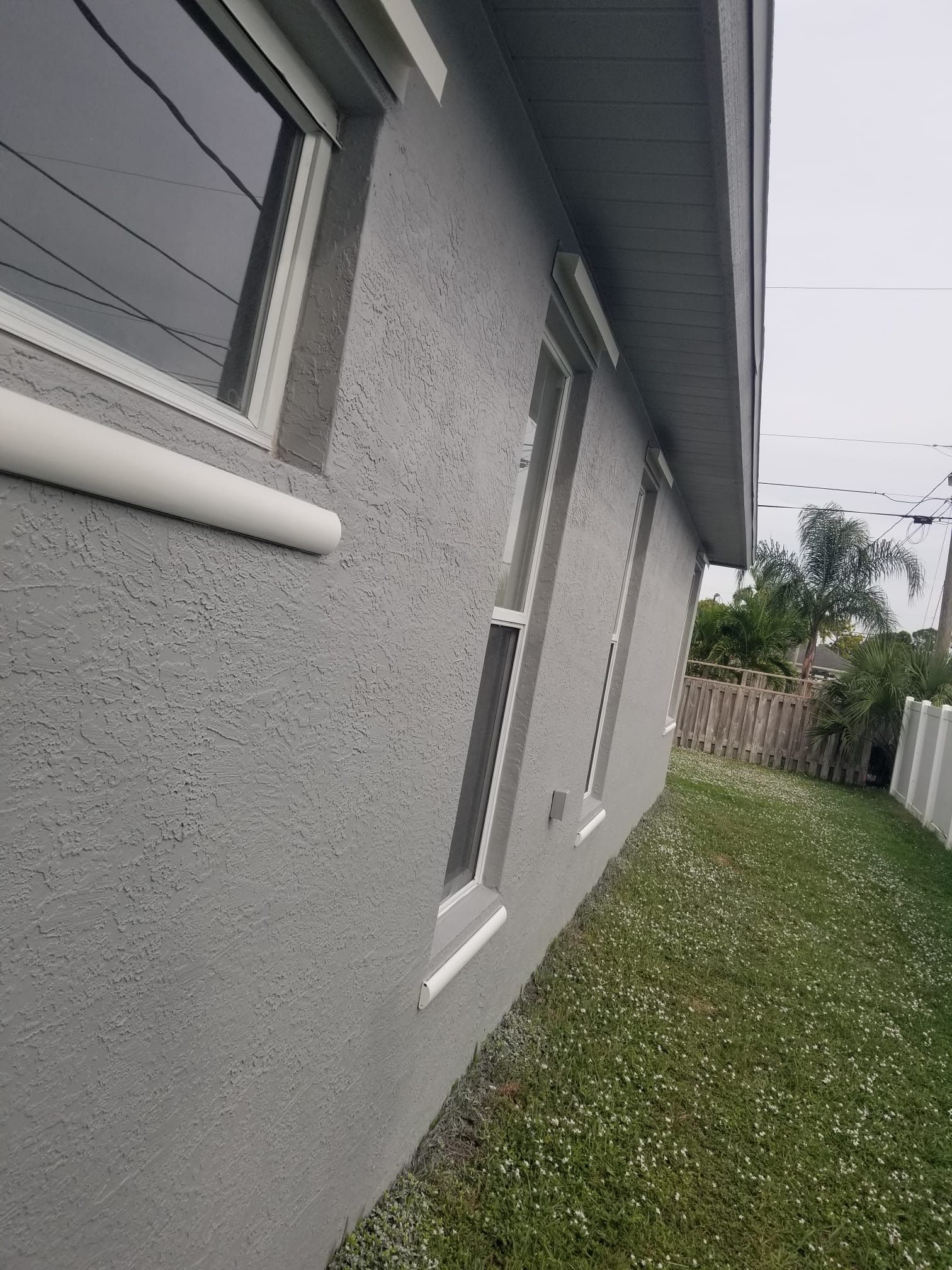 Gray stucco house exterior with windows, lawn, and fence.
