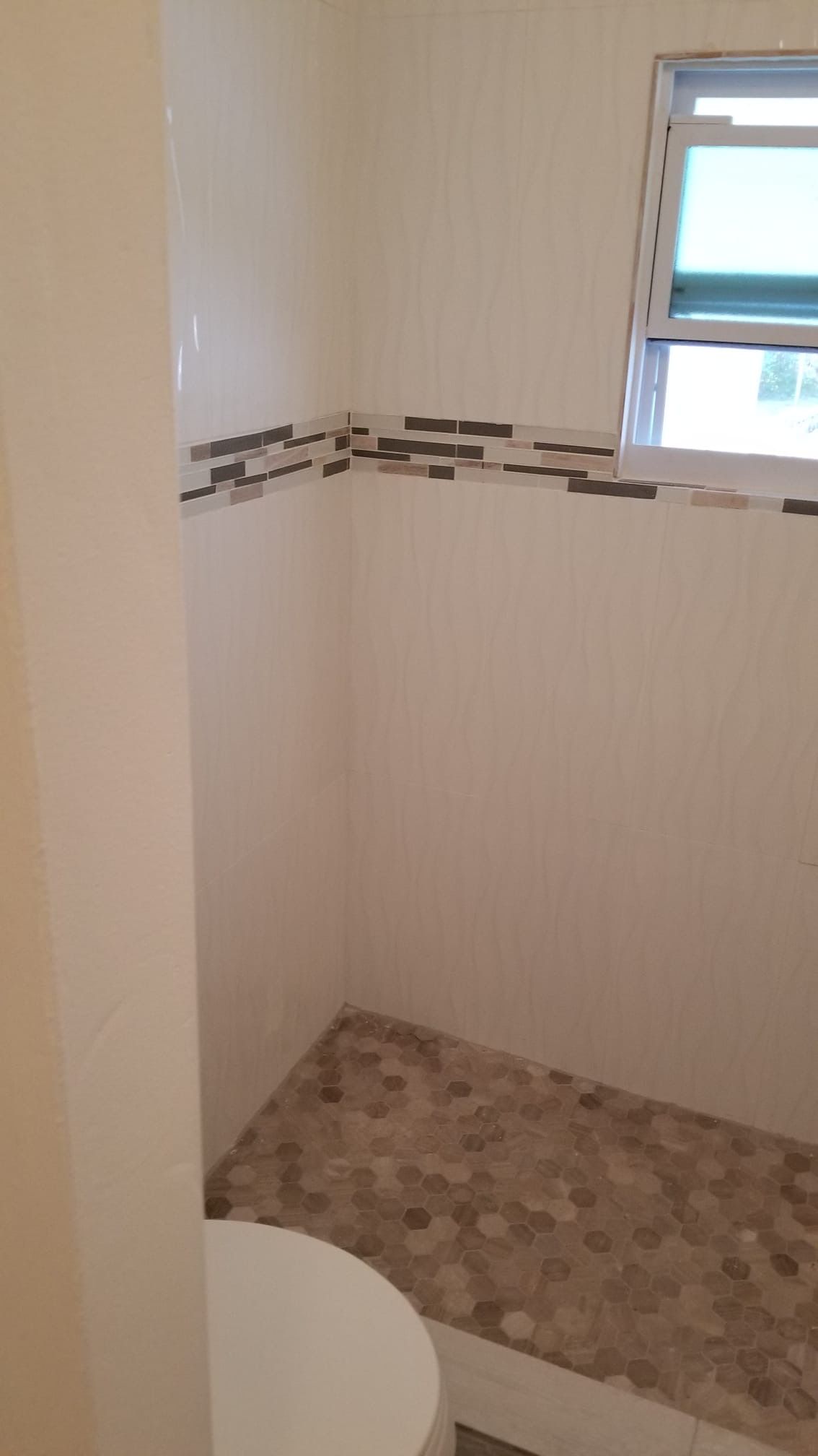 Small shower with pebble floor and tile accent near a window.
