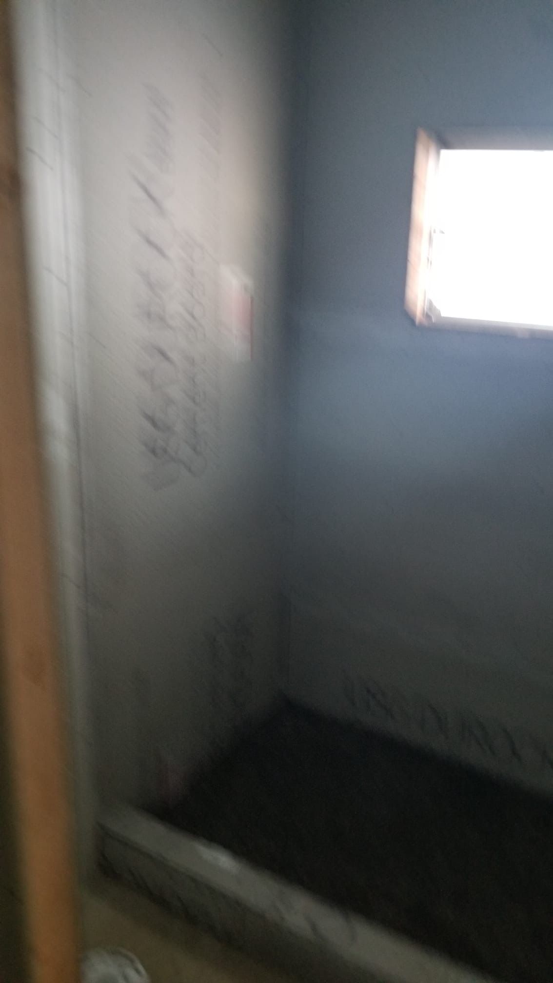 Interior of a small room with a window, unfinished walls, and a shower base.