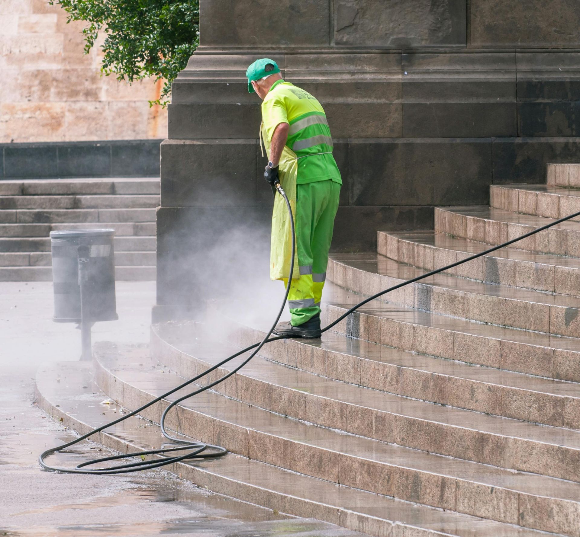 Person in green cleaning steps with a pressure washer; water spray visible.