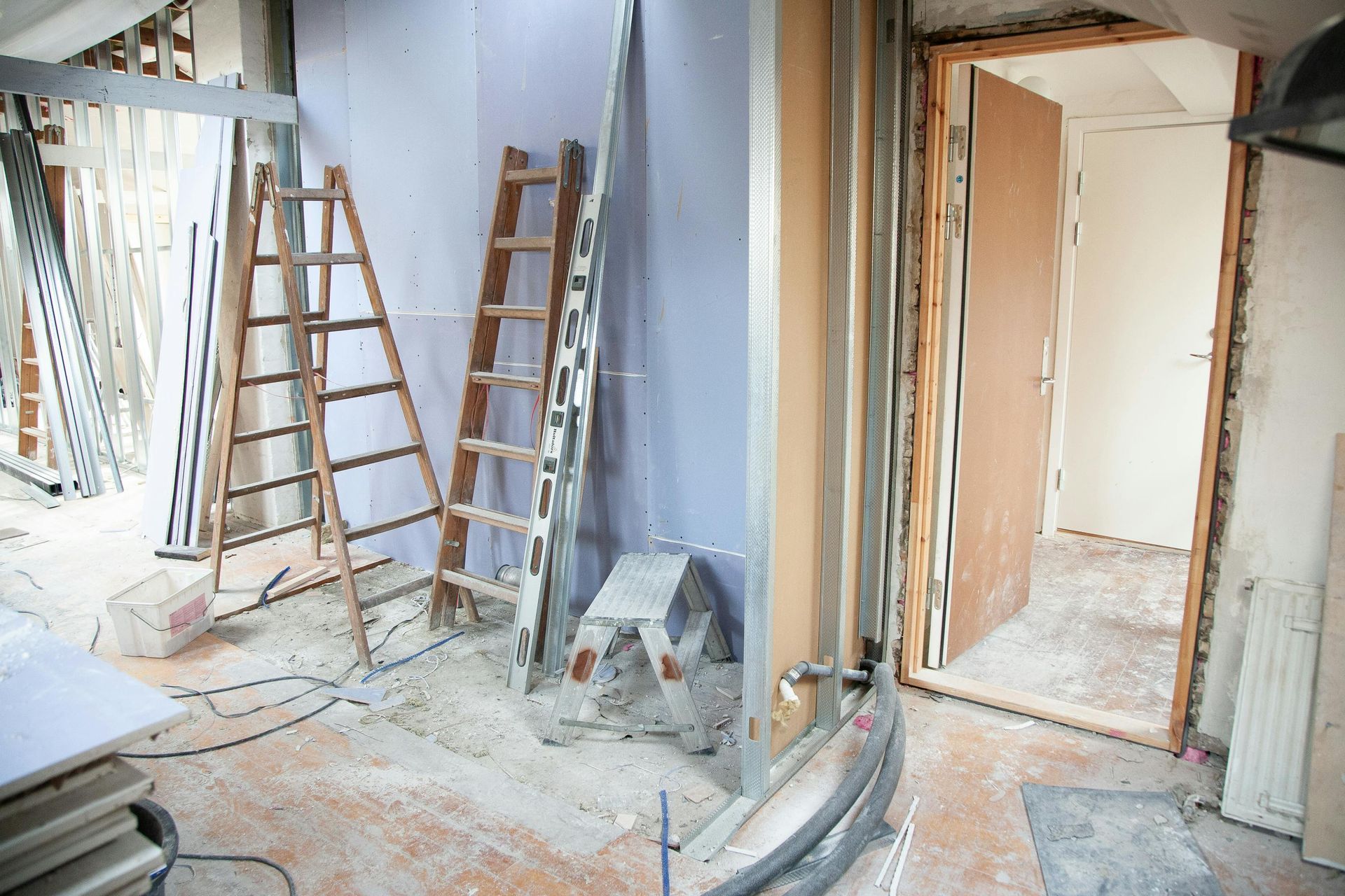 Interior room under construction with ladders, drywall, and doorway.
